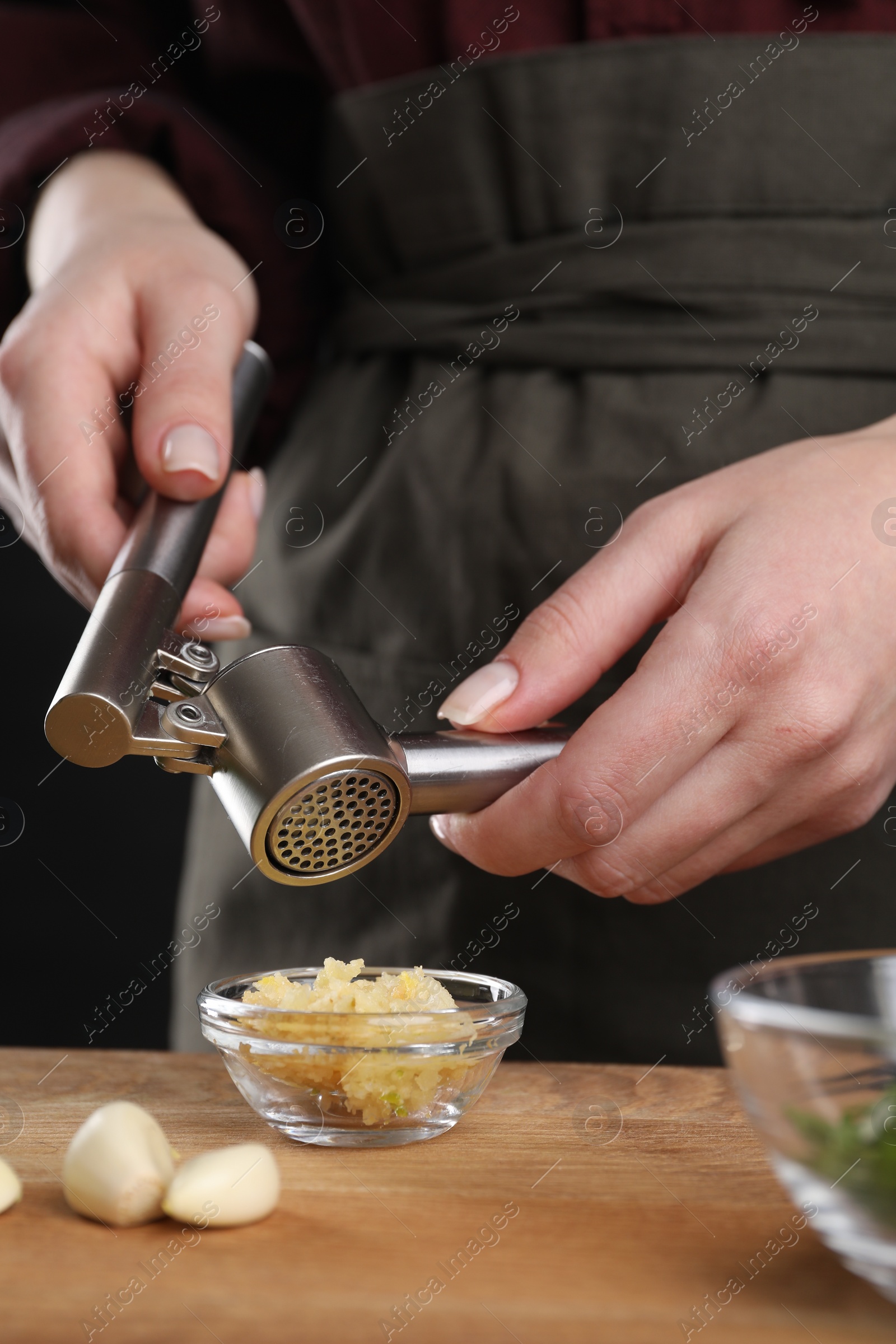 Photo of Woman squeezing garlic with press at wooden table, closeup