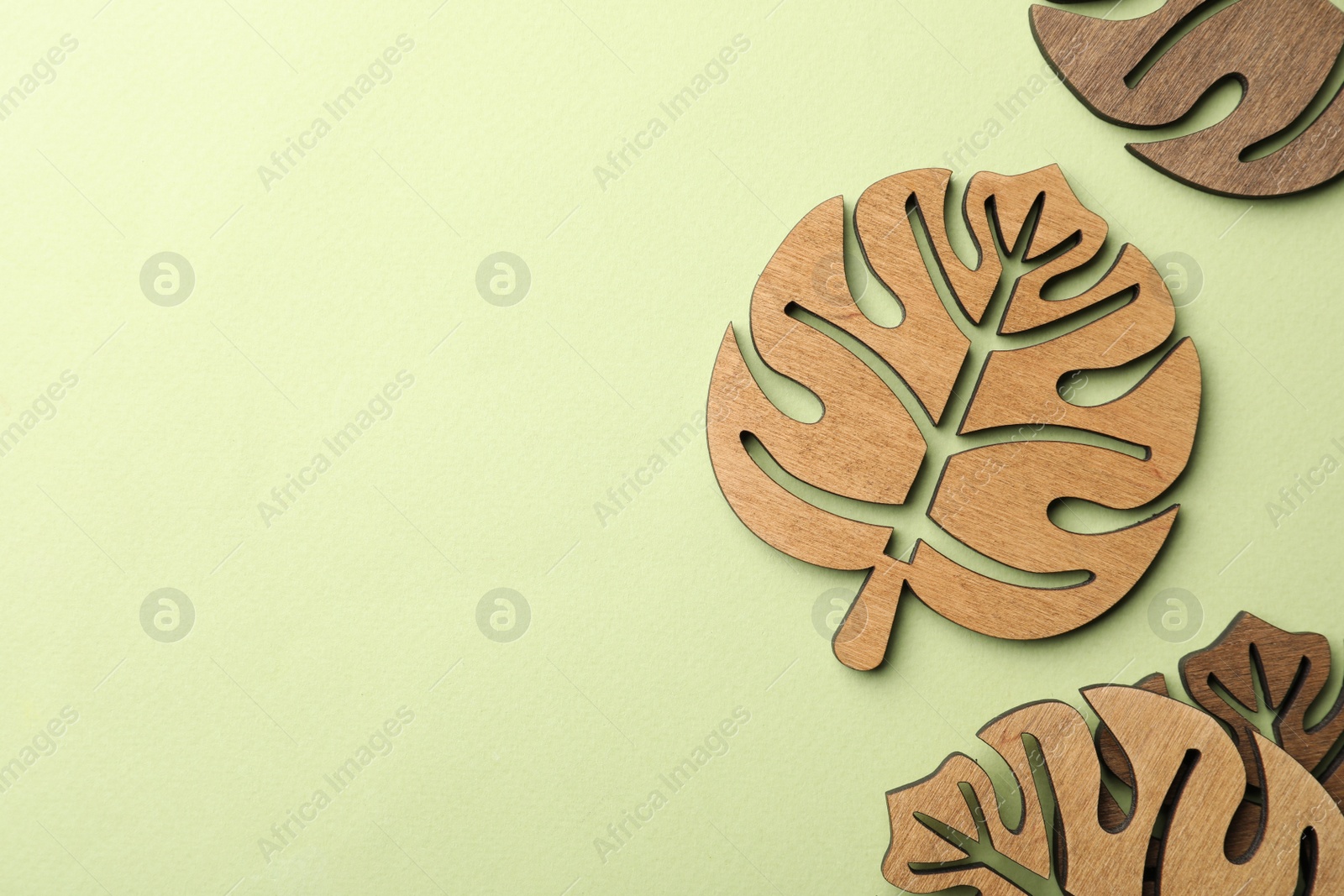 Photo of Leaf shaped wooden cup coasters on green background, flat lay. Space for text