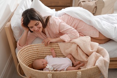 Photo of Happy young mother resting near cradle with sleeping newborn baby at home