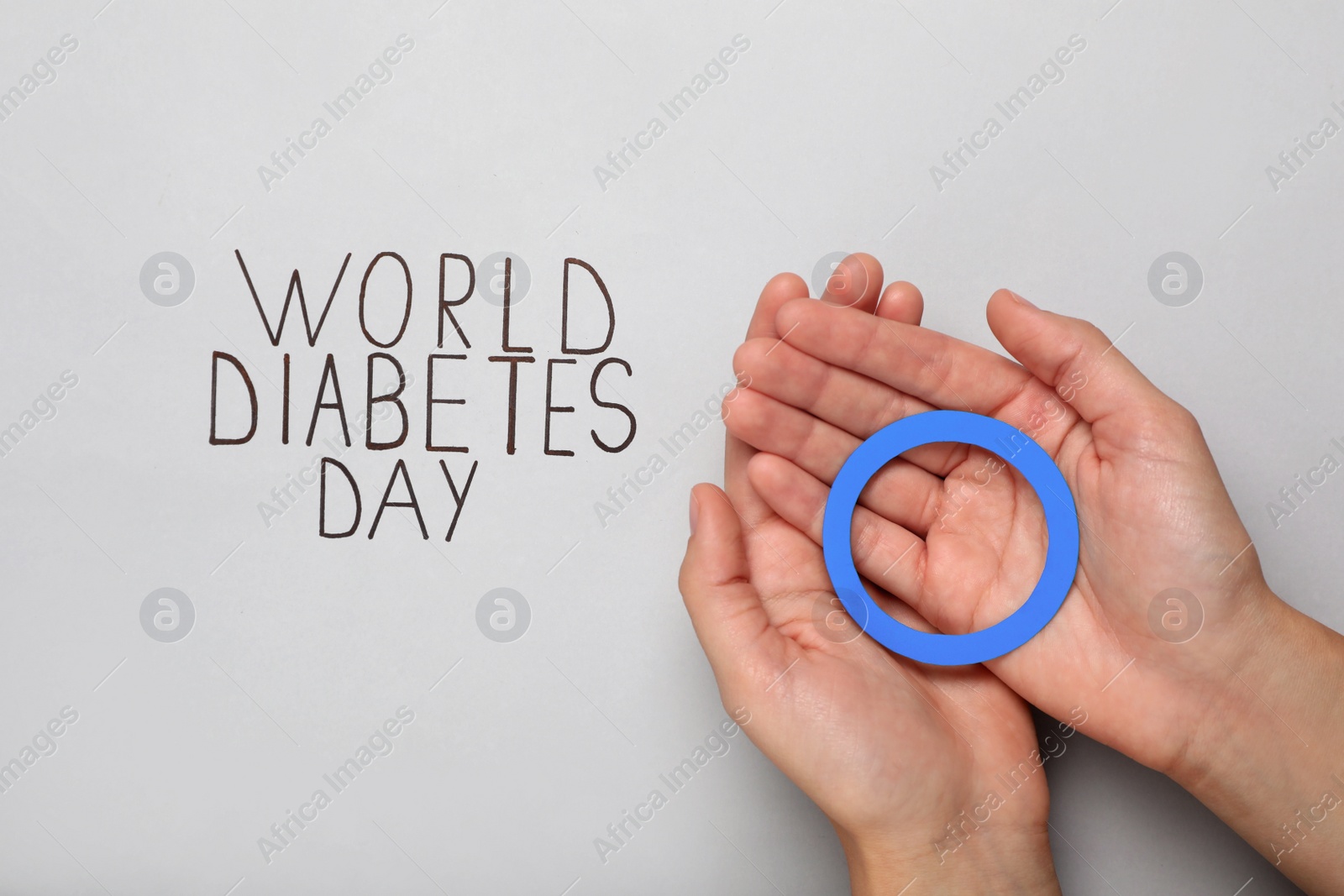 Photo of Woman holding blue paper circle near text World Diabetes Day on light background, top view