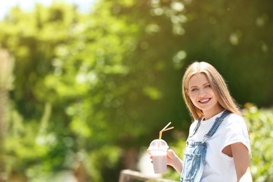 Young woman with cup of delicious milk shake outdoors