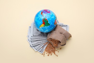 Photo of Import and export concept. Globe, bag of wheat grains and banknotes on beige background, flat lay