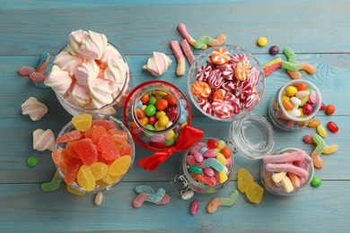 Photo of Jars with different delicious candies on light blue wooden table, flat lay