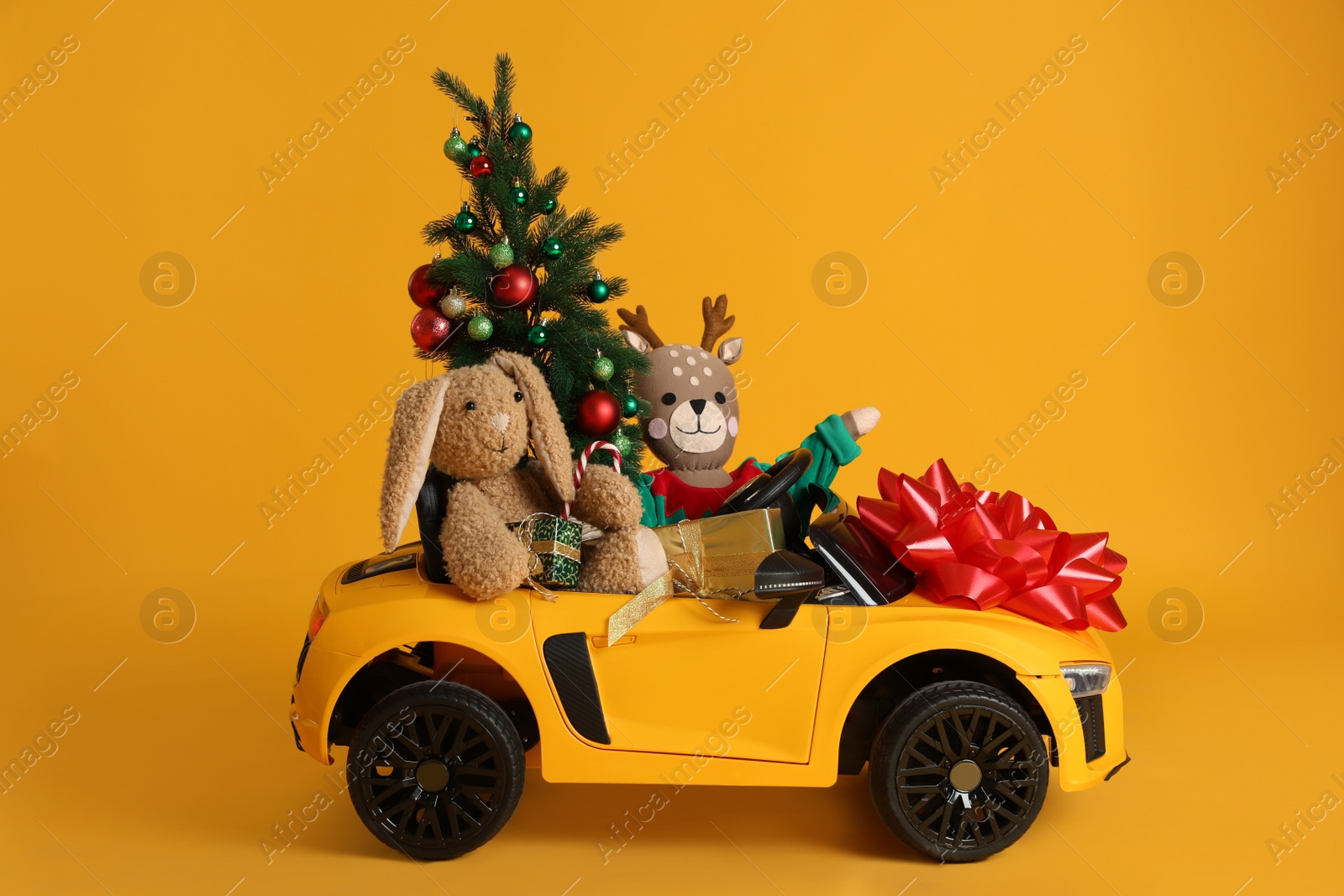 Photo of Child's electric car with toys, gift boxes and Christmas tree on orange background