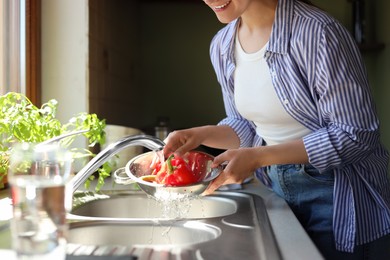 Photo of Woman washing fresh bell peppers in kitchen sink, closeup