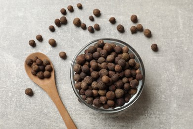 Aromatic allspice pepper grains in bowl and spoon on grey table, flat lay
