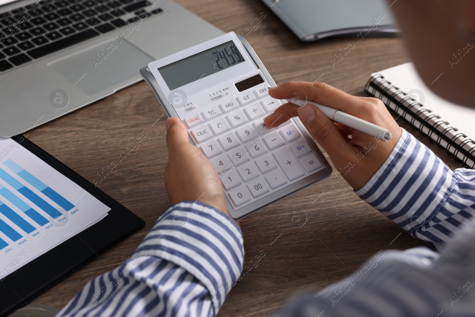 Photo of Woman using calculator at wooden table, closeup