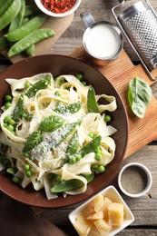 Delicious pasta with green peas and ingredients on wooden table, flat lay