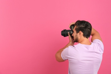 Photo of Young professional photographer taking picture on pink background. Space for text