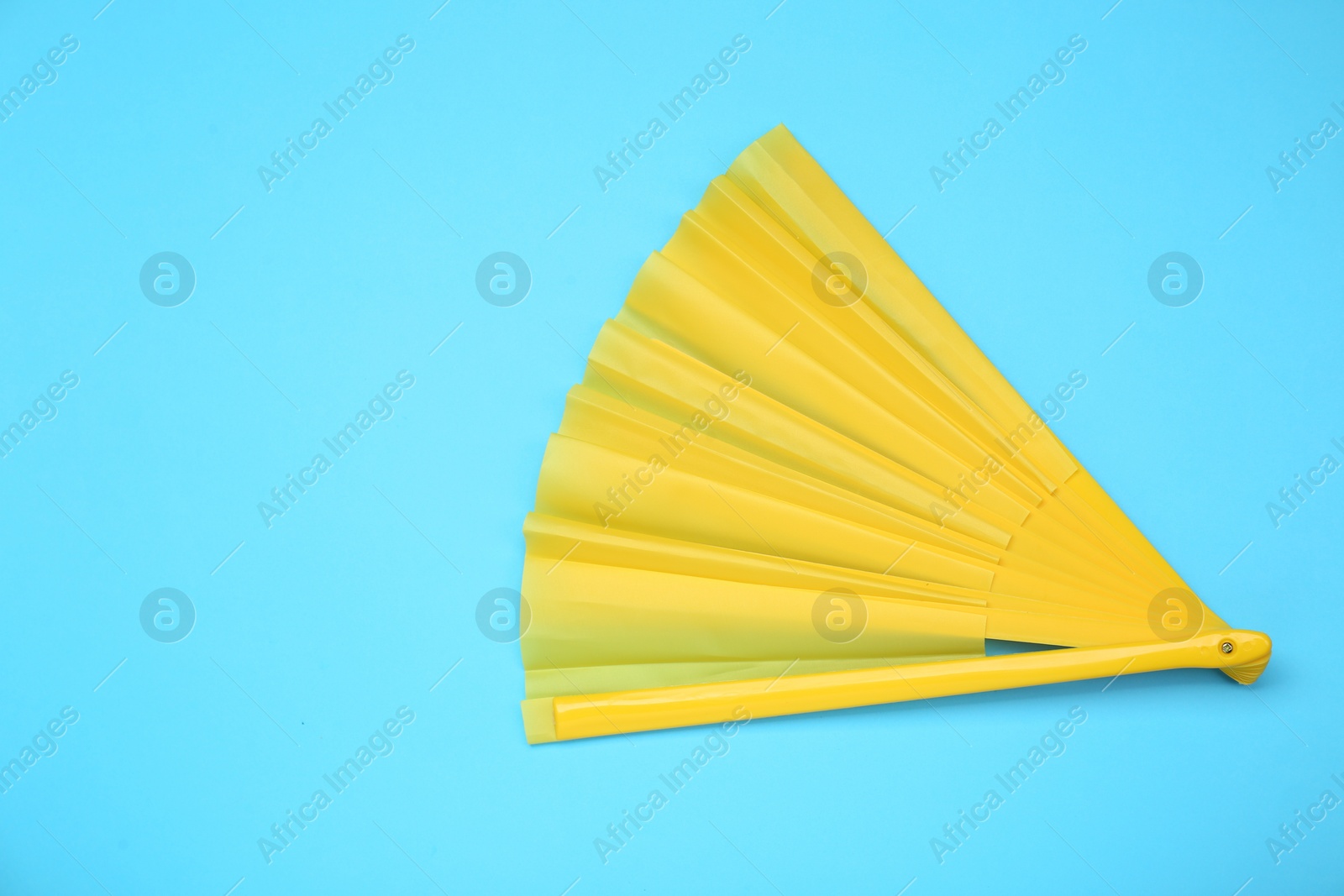 Photo of Bright yellow hand fan on light blue background, top view. Space for text