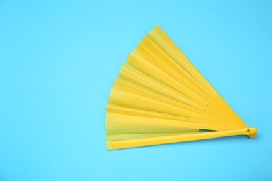 Photo of Bright yellow hand fan on light blue background, top view. Space for text