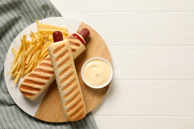 Photo of Delicious french hot dogs, fries and dip sauce on white wooden table, top view. Space for text