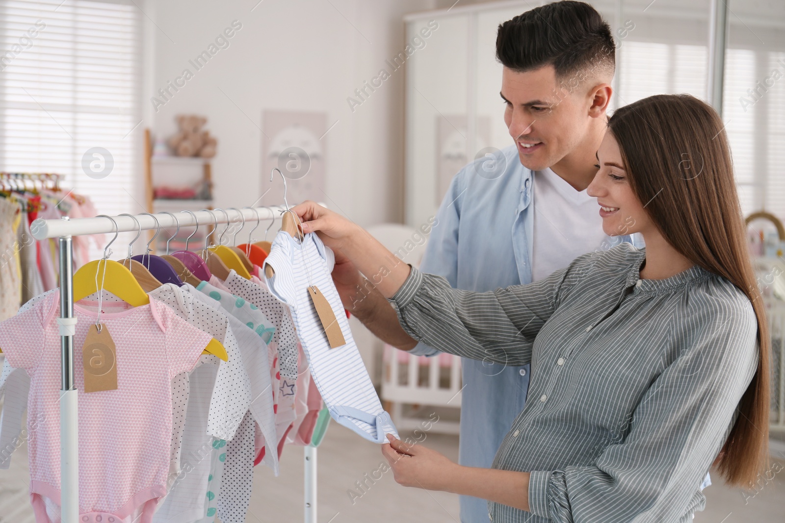 Photo of Happy pregnant woman with her husband choosing baby clothes in store. Shopping concept