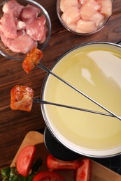 Fondue pot, forks with fried meat pieces and other products on wooden table, flat lay