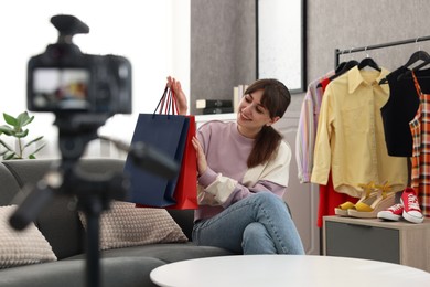 Smiling fashion blogger with shopping bags recording video at home