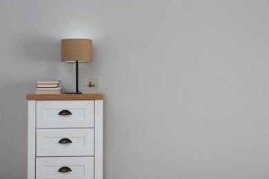 Photo of Chest of drawers with lamp, books and clock near light wall, space for text. Interior design
