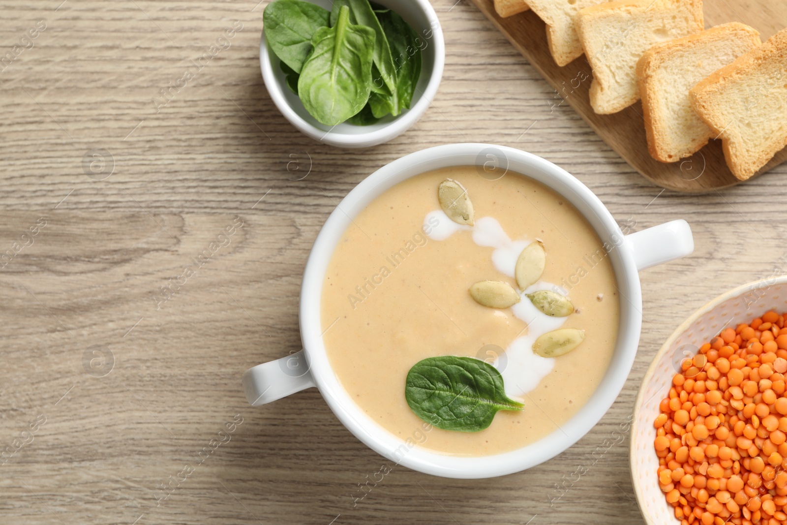 Photo of Healthy cream soup high in vegetable fats, bread and spinach on wooden table, flat lay. Space for text