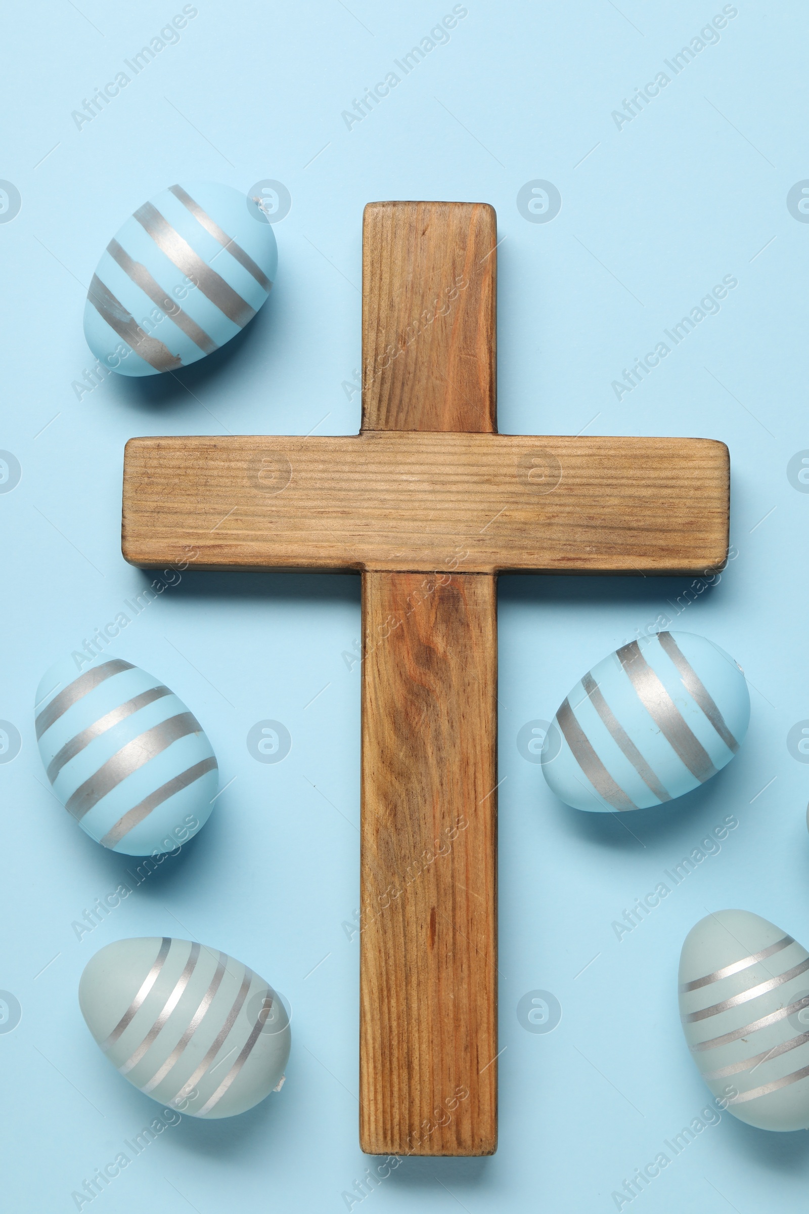 Photo of Wooden cross and painted Easter eggs on light blue background, flat lay