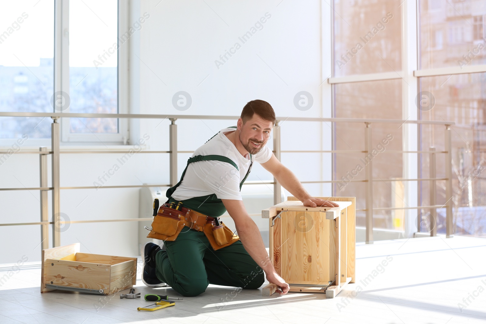 Photo of Handyman in uniform assembling furniture indoors. Professional construction tools