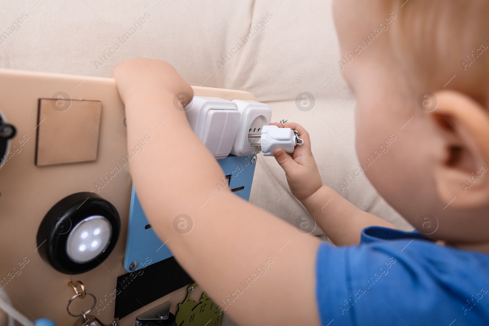 Photo of Cute little boy playing with busy board on sofa, closeup