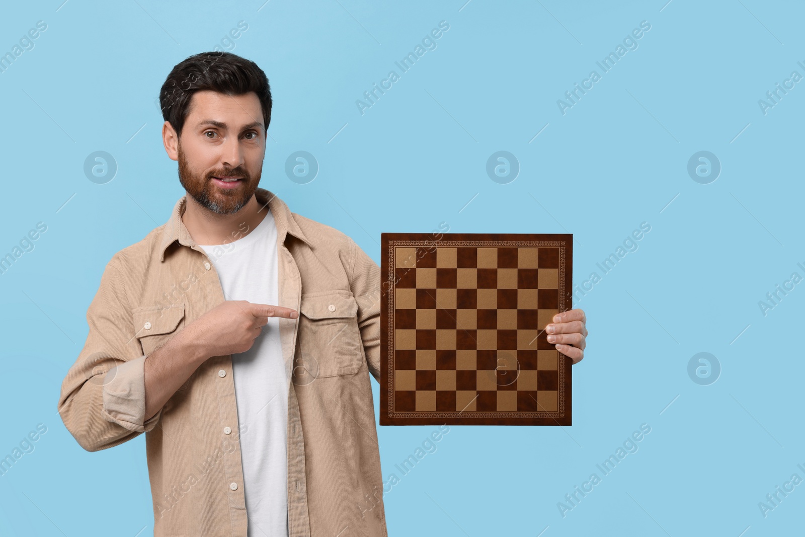 Photo of Handsome man showing chessboard on light blue background