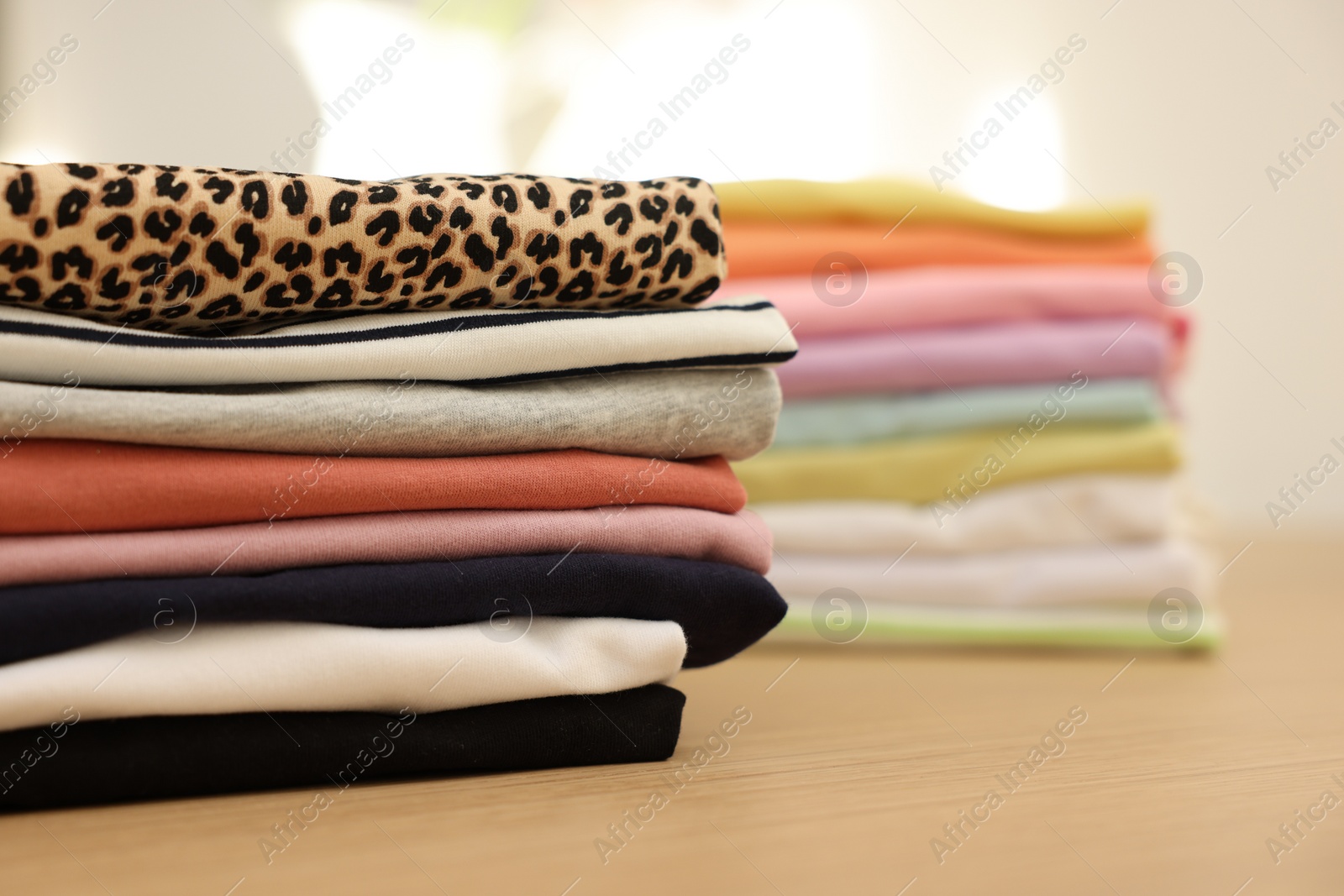 Photo of Many stacked clean clothes on wooden table, closeup