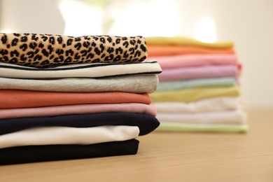 Photo of Many stacked clean clothes on wooden table, closeup