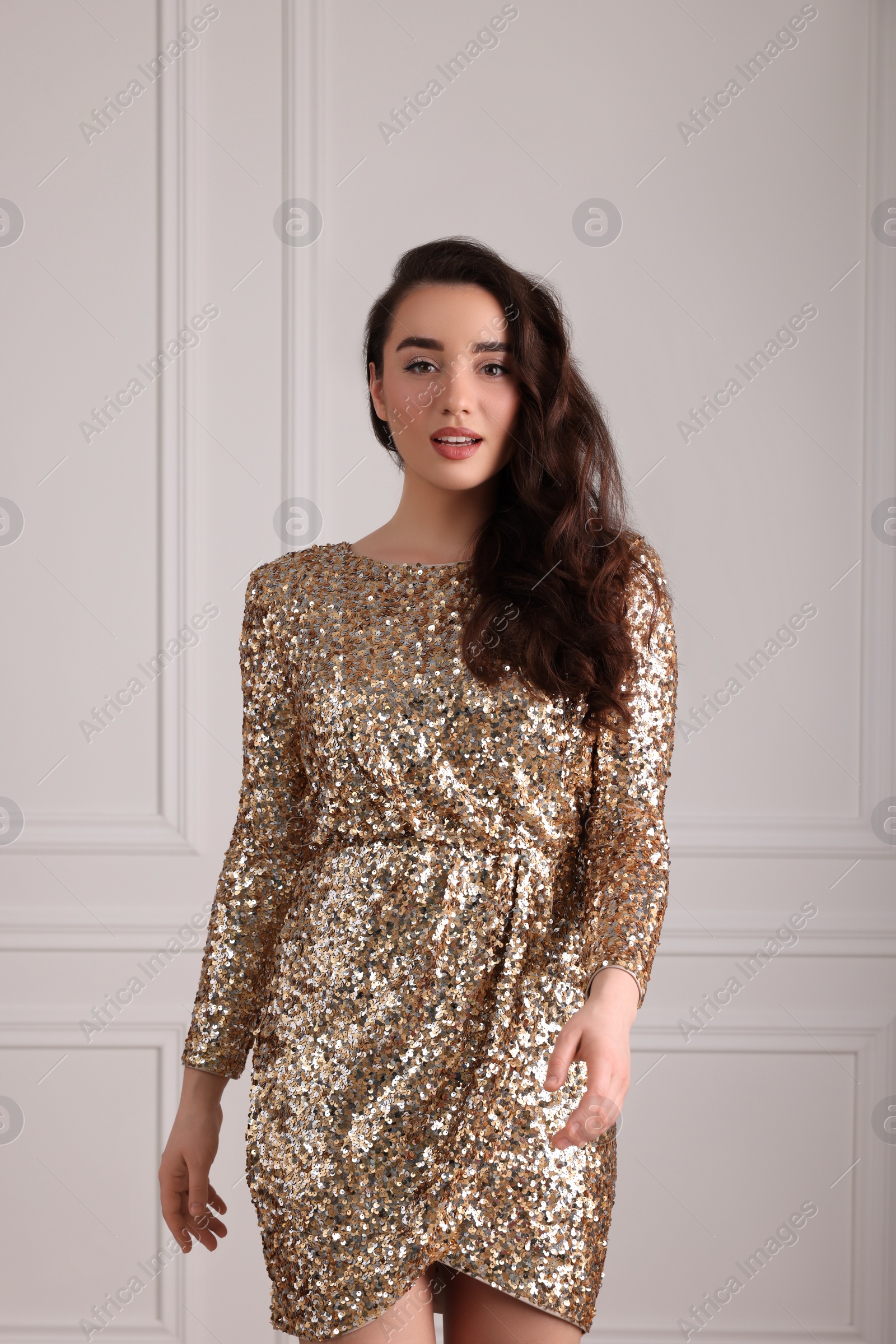 Photo of Beautiful woman in elegant glitter dress near white wall