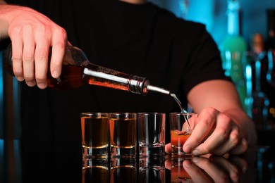 Bartender pouring alcohol drink into shot glass at mirror counter in bar, closeup