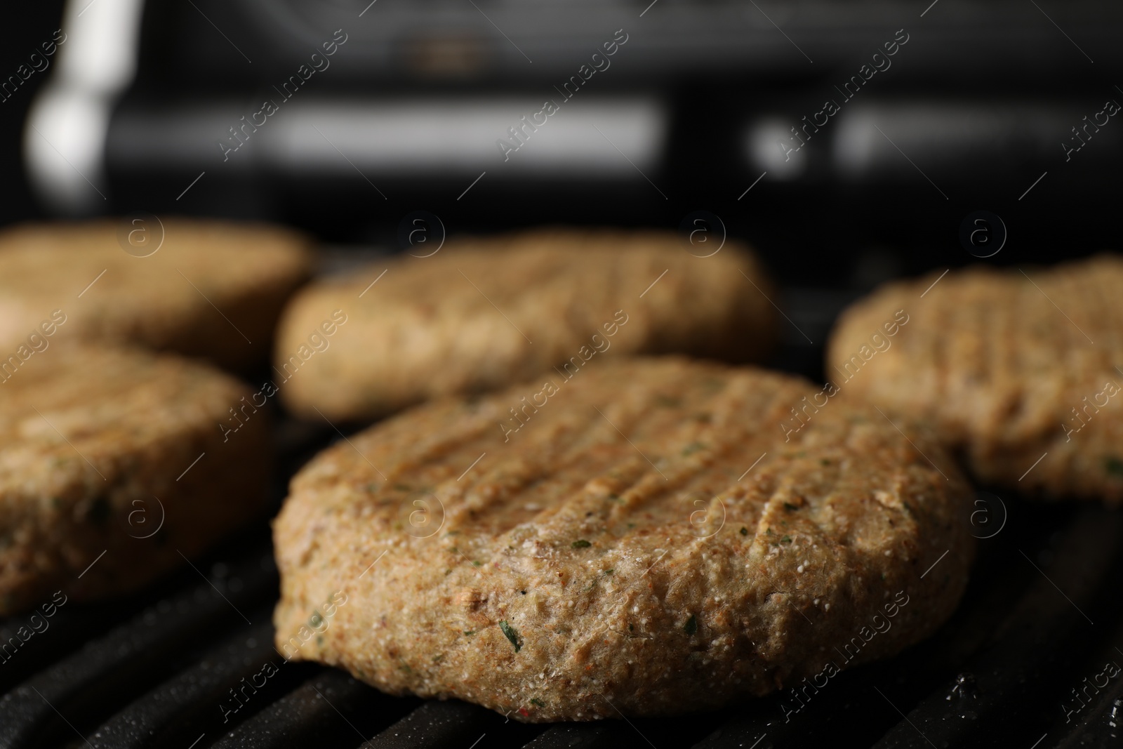 Photo of Delicious vegan cutlets cooking on electric grill, closeup