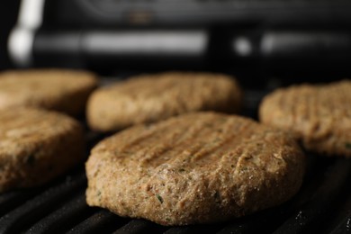 Photo of Delicious vegan cutlets cooking on electric grill, closeup