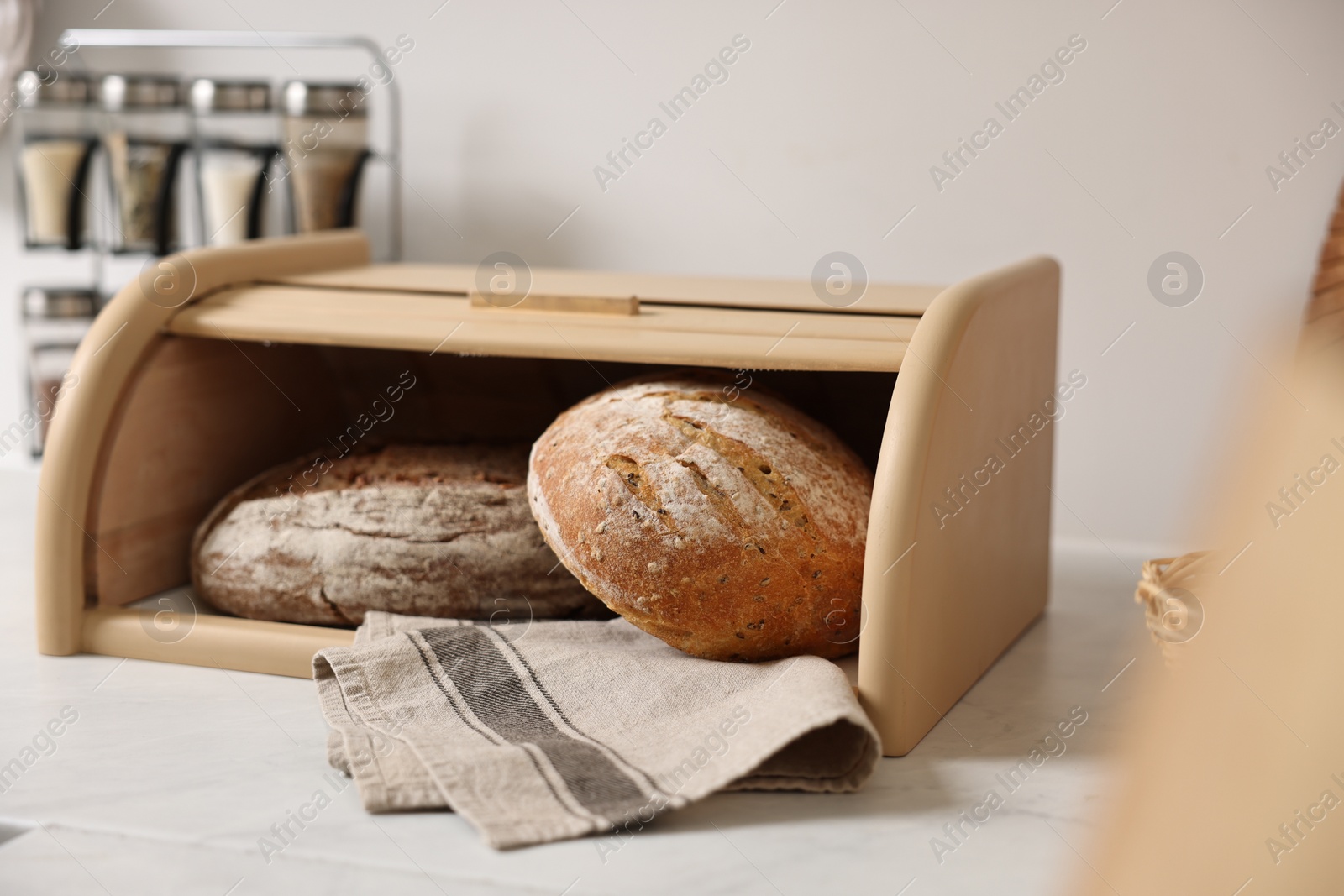 Photo of Wooden bread basket with freshly baked loaves on white marble table in kitchen