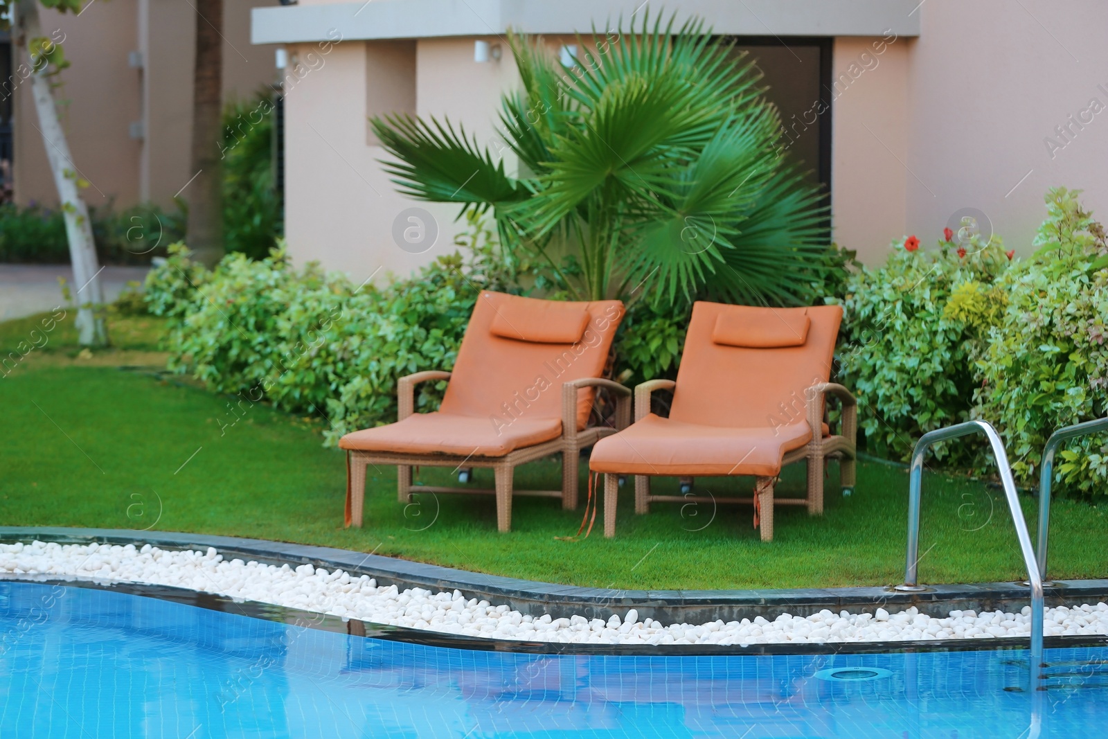 Photo of Sunbeds near modern swimming pool with stairs at resort