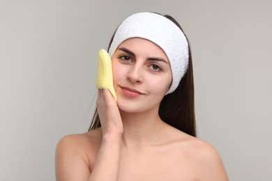 Photo of Young woman with headband washing her face using sponge on light grey background