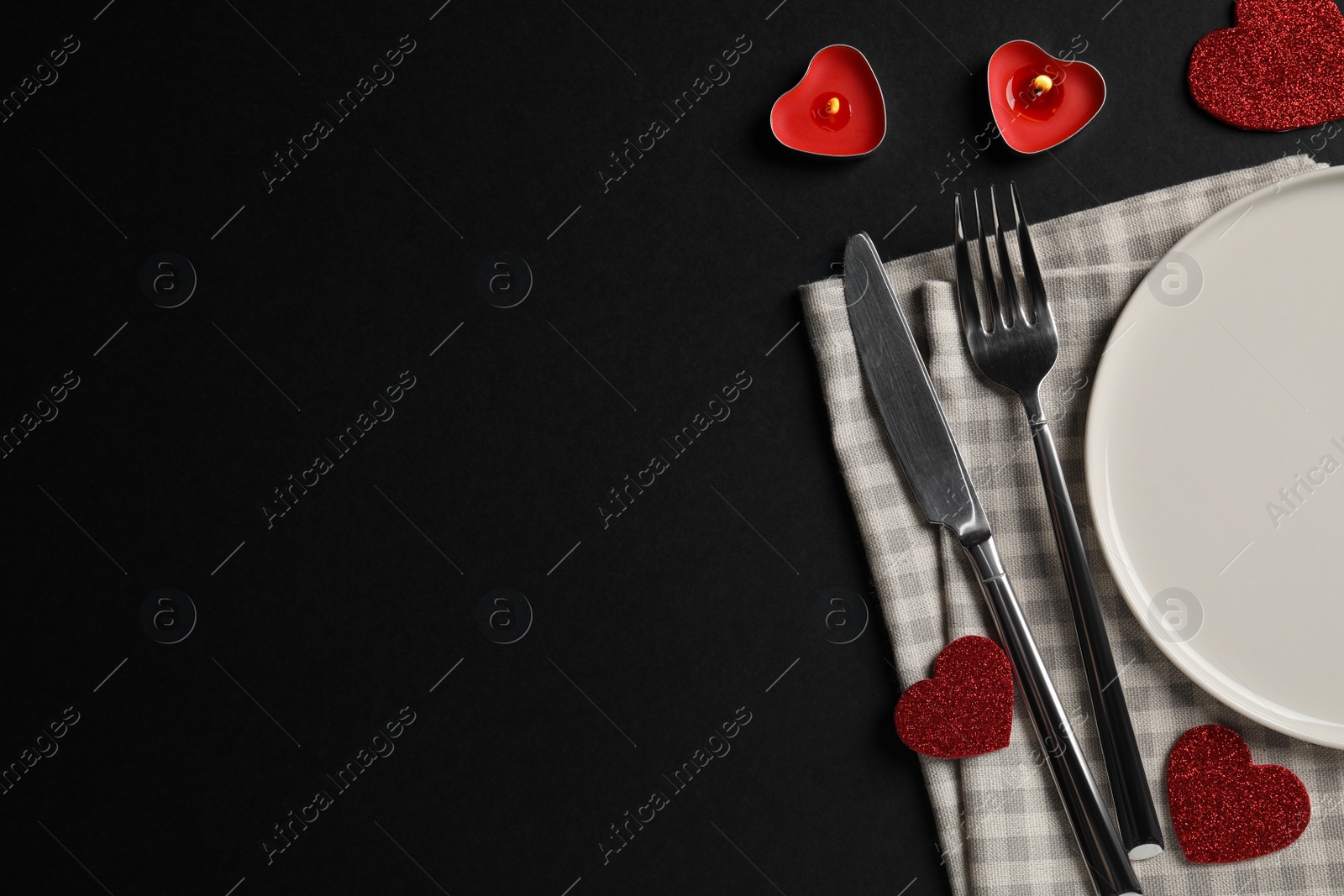 Photo of Beautiful place setting with dishware, burning candles and decorative hearts on black table for romantic dinner, flat lay. Space for text