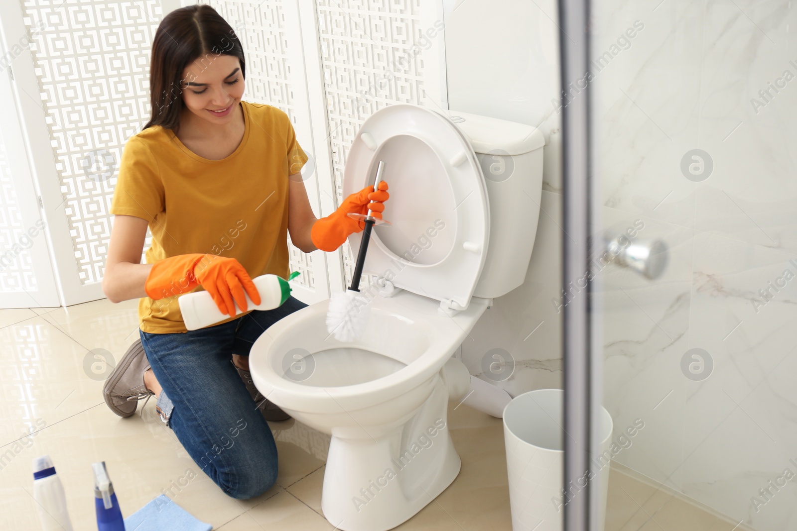 Photo of Young woman cleaning toilet bowl in bathroom