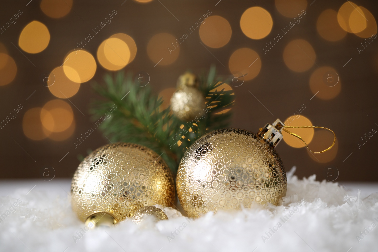 Photo of Beautiful Christmas balls and fir branch on snow against blurred festive lights