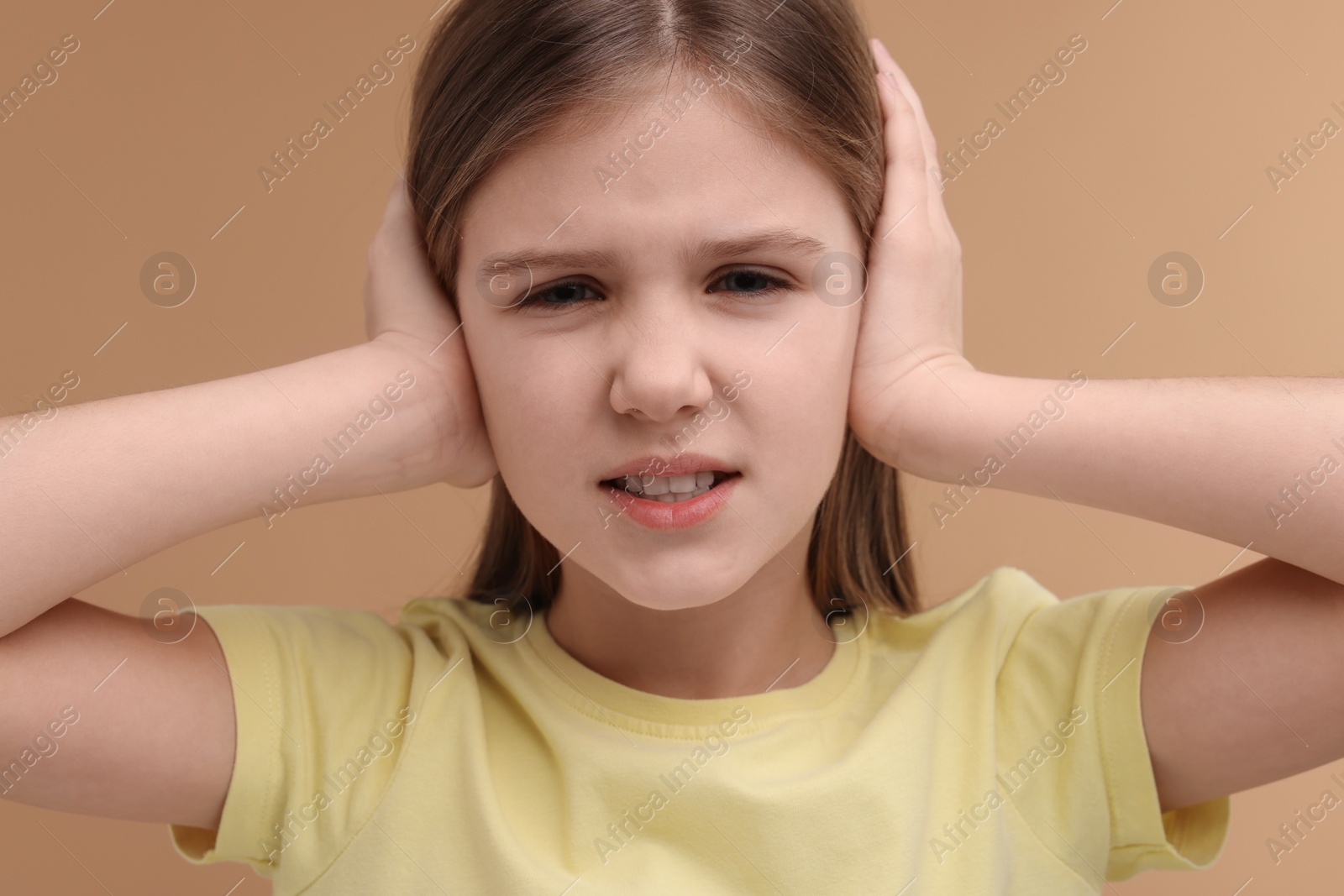 Photo of Hearing problem. Little girl suffering from ear pain on pale brown background