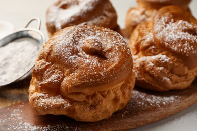 Photo of Delicious profiteroles with powdered sugar on wooden board, closeup