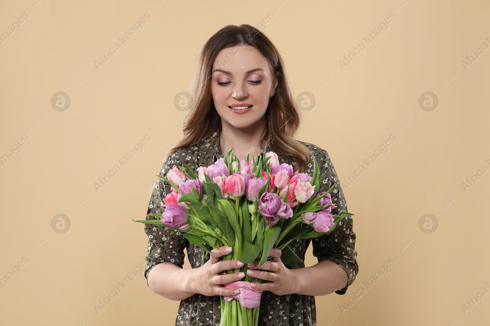 Photo of Happy young woman holding bouquet of beautiful tulips on beige background