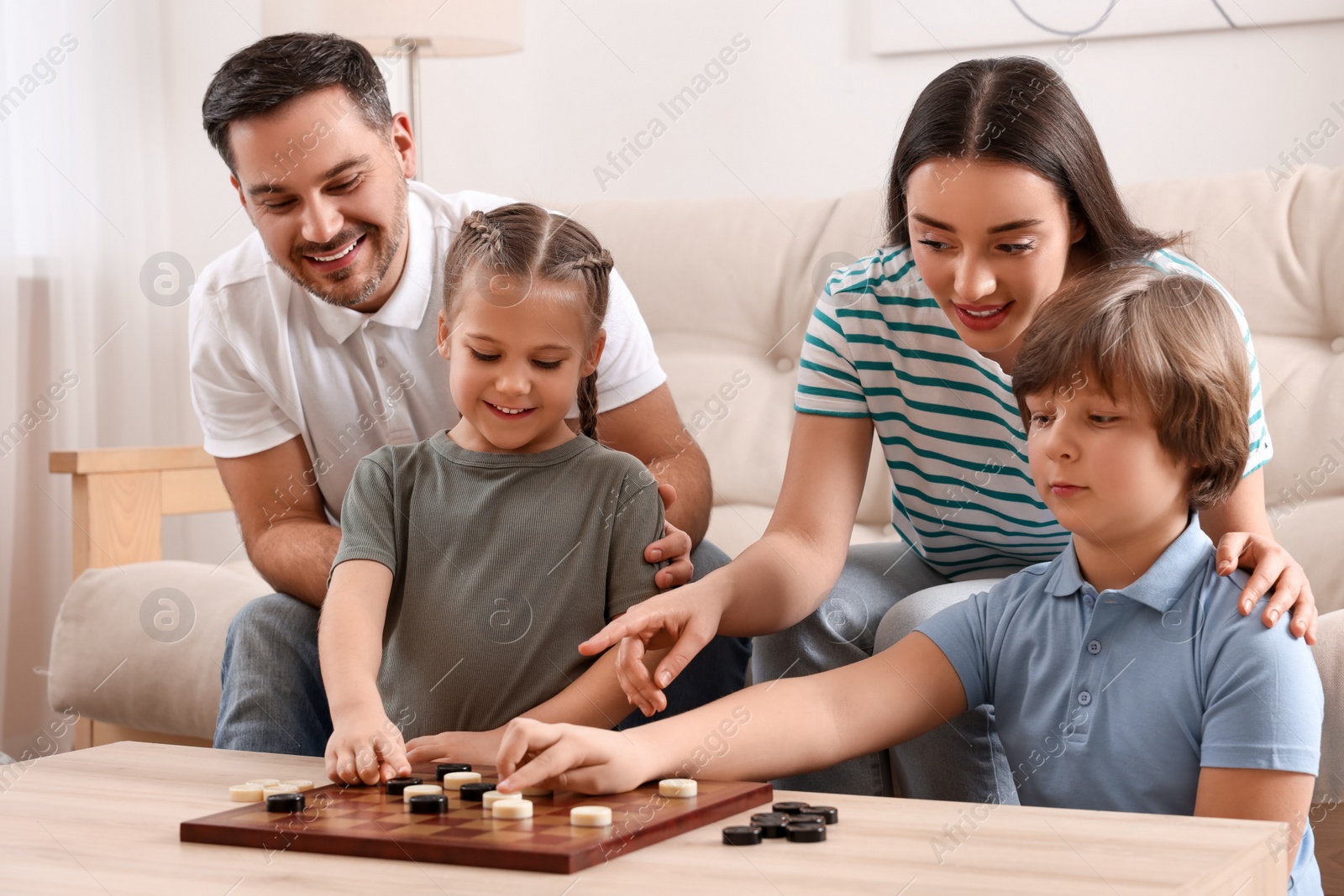 Photo of Parents playing checkers with children at table in room