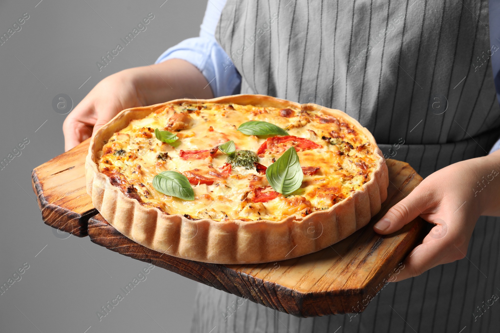 Photo of Woman holding board with tasty quiche on grey background, closeup