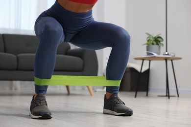 Photo of Woman doing squats with fitness elastic band at home, closeup