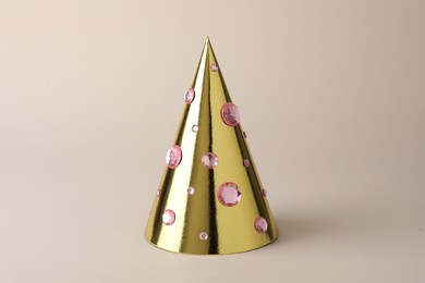 Photo of One shiny golden party hat with rhinestones on beige background