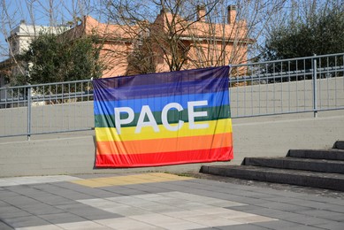 Beautiful rainbow peace flag with word PACE hanging on metal railing outdoors