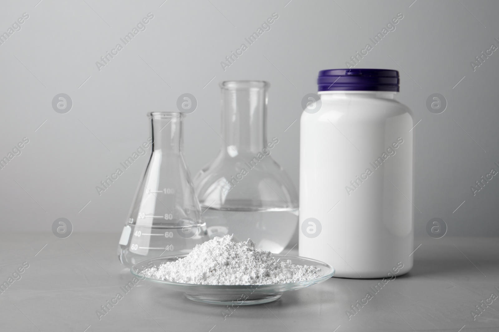 Photo of Plate with calcium carbonate powder, jar and laboratory glassware on grey table