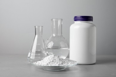Photo of Plate with calcium carbonate powder, jar and laboratory glassware on grey table