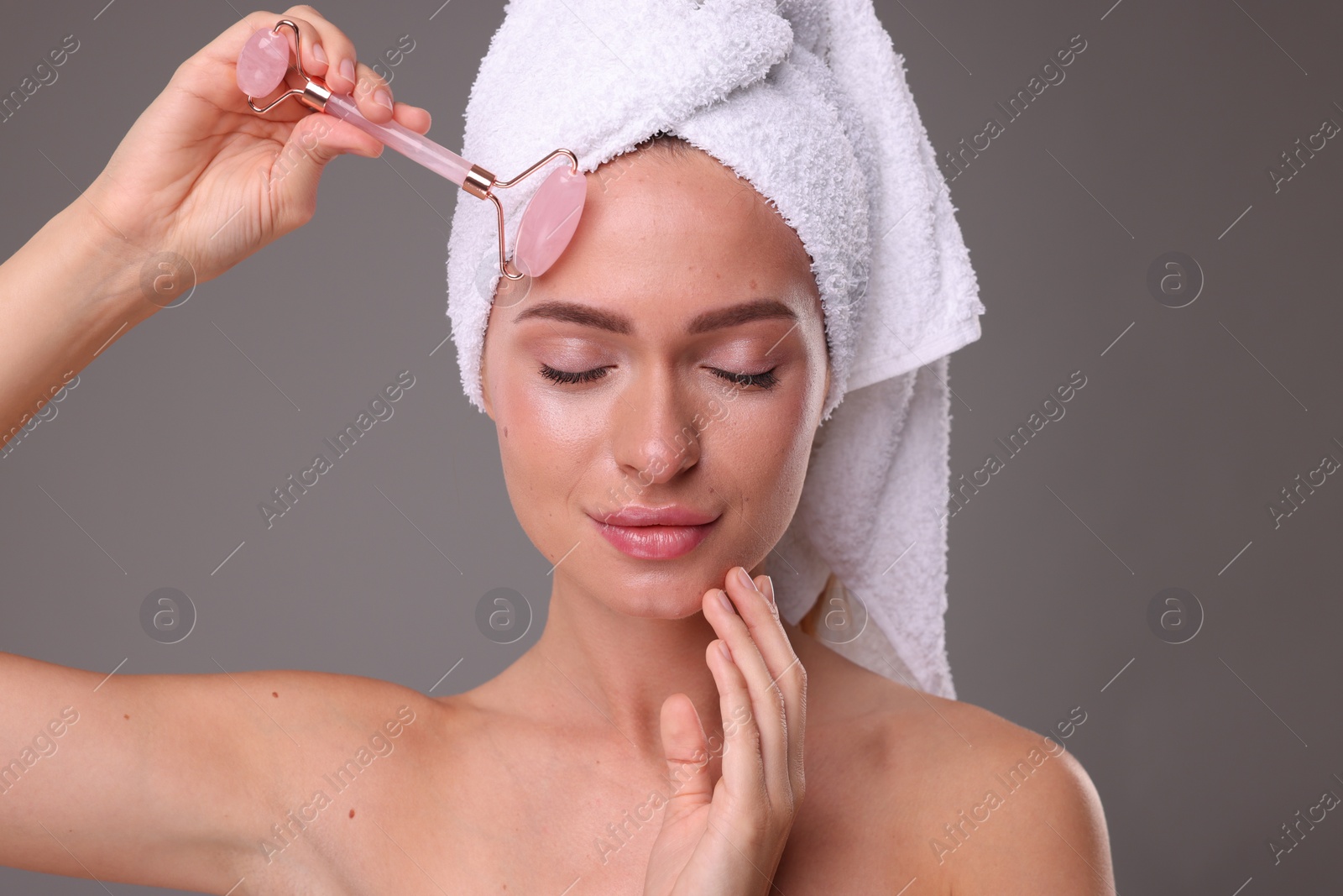 Photo of Young woman massaging her face with rose quartz roller on grey background