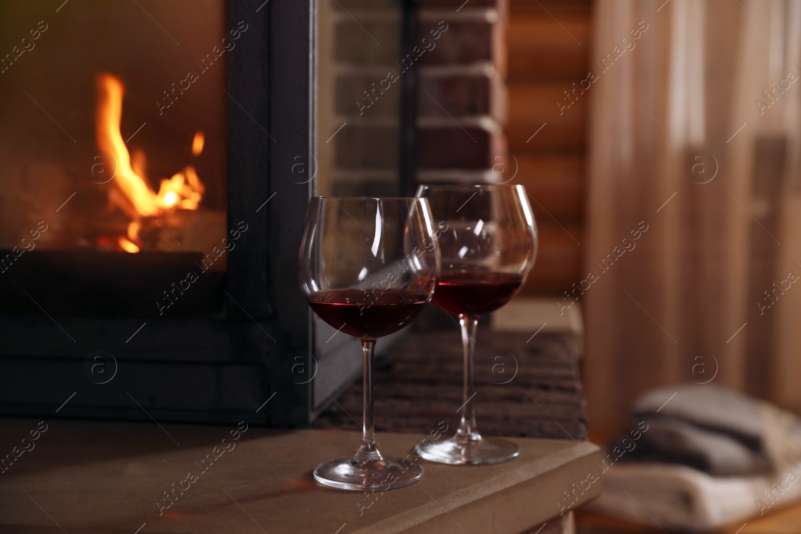 Photo of Glasses of wine near fireplace indoors. Winter vacation
