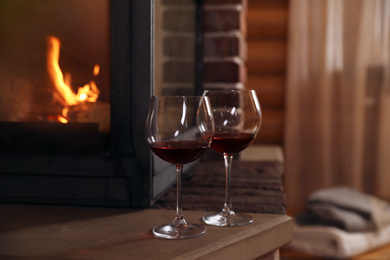 Photo of Glasses of wine near fireplace indoors. Winter vacation